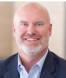 A bald man with a beard is wearing a suit and smiling. KENNY OWEN