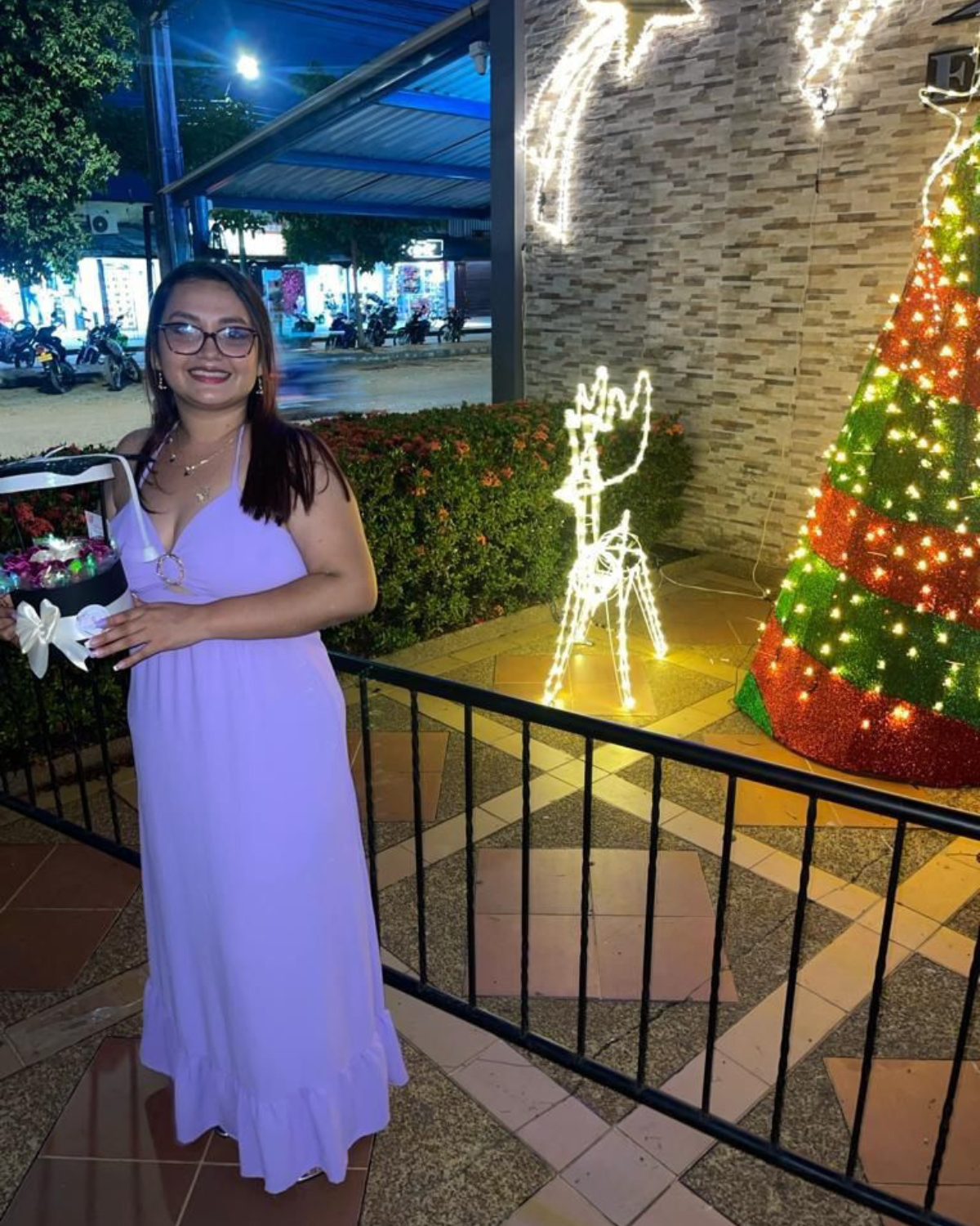 Yeimmy Paola Grenados in a purple dress is standing in front of a christmas tree. osf fundamor colombia andy stein