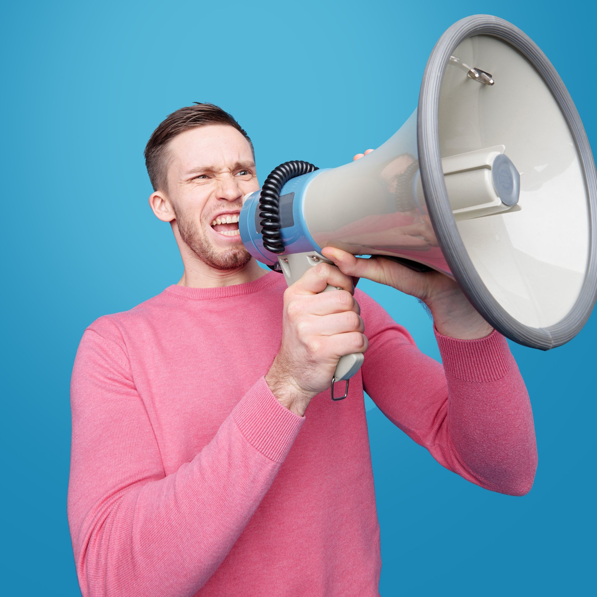 A man in a pink sweater is holding a megaphone