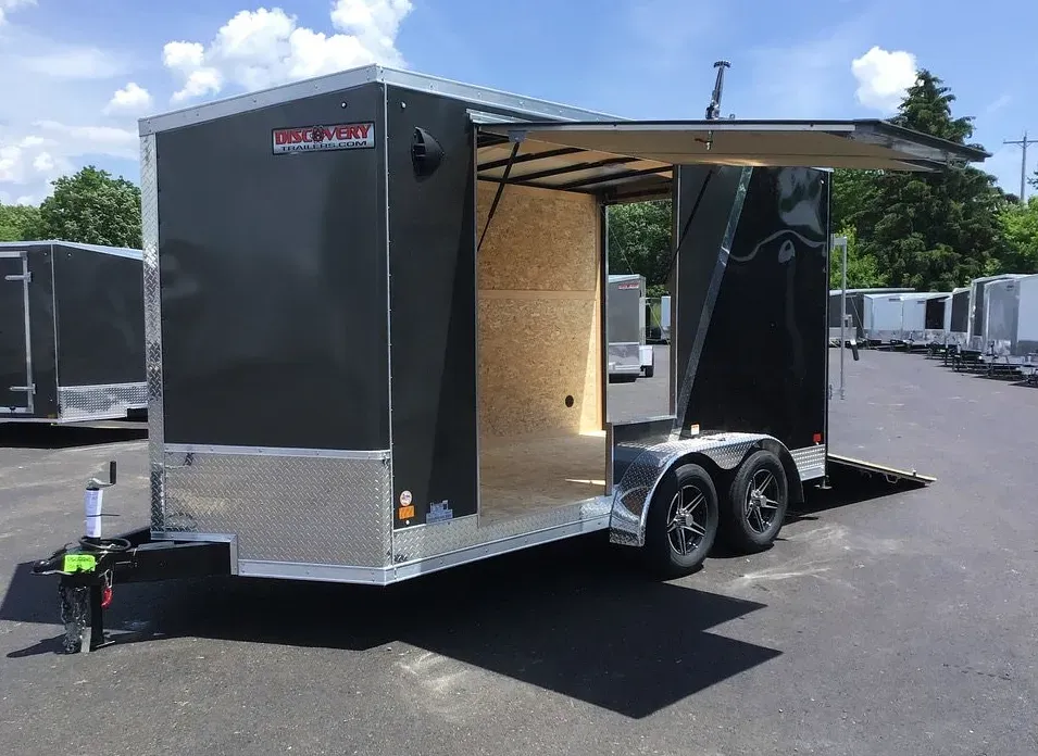 Black enclosed trailer with rear ramp door open, parked on pavement in daylight