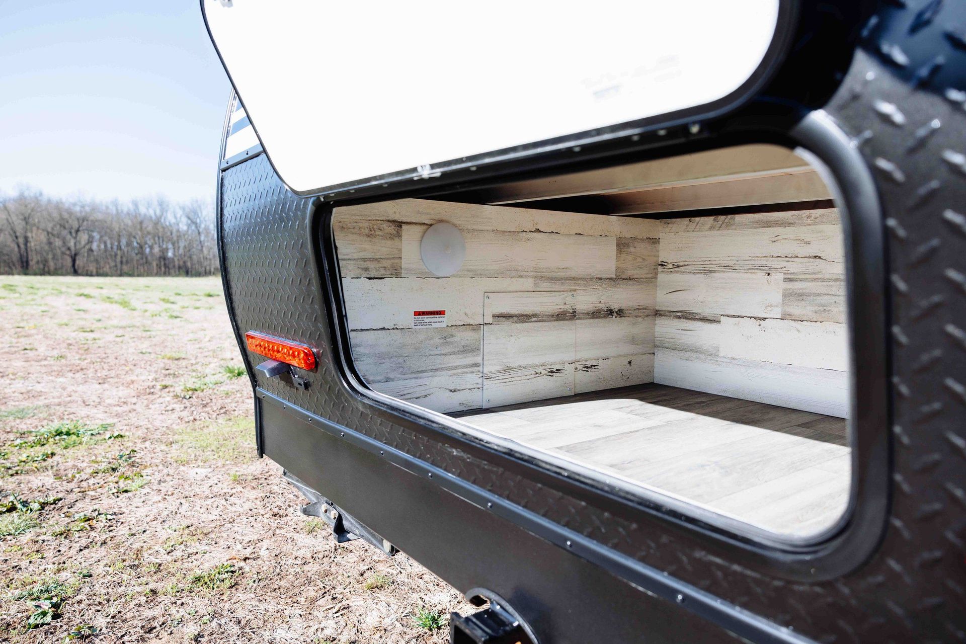 Open rear storage compartment of a black camper trailer with light wood interior.