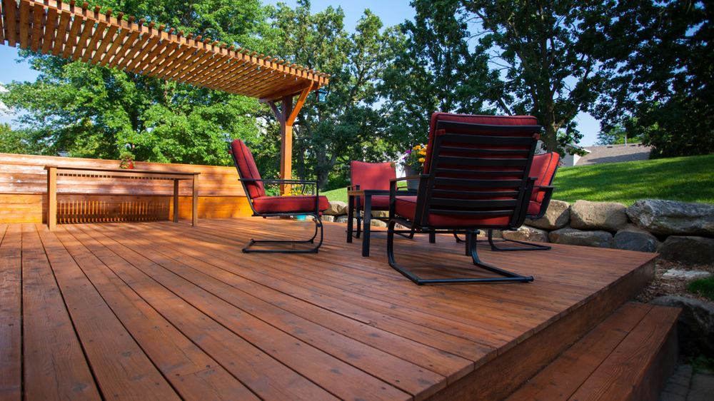 Wooden deck with red chairs, pergola, and surrounding greenery.