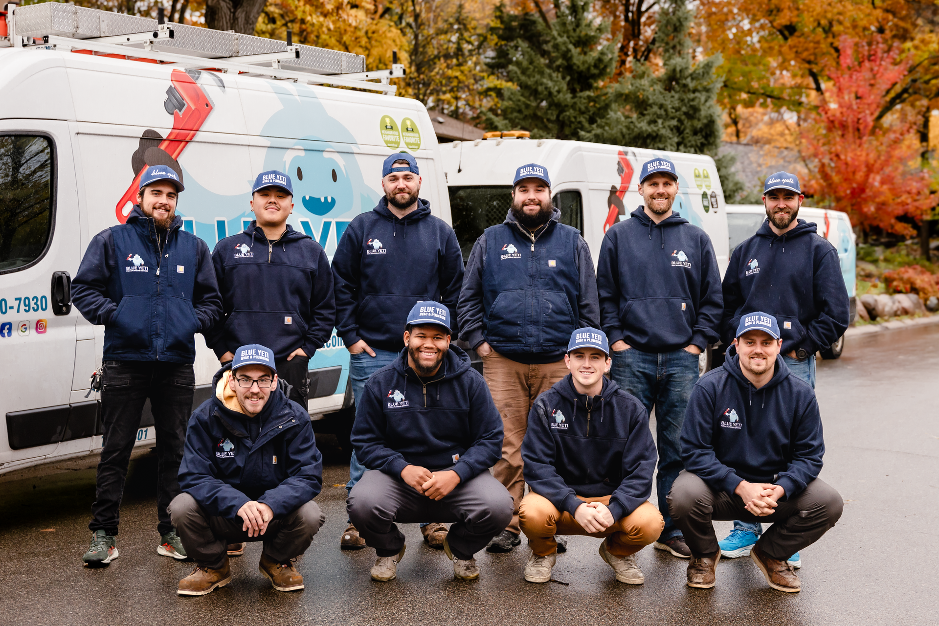 Team of Blue Yeti HVAC Plumbing HVAC technicians in navy blue sweatshirts posing in front of company vans