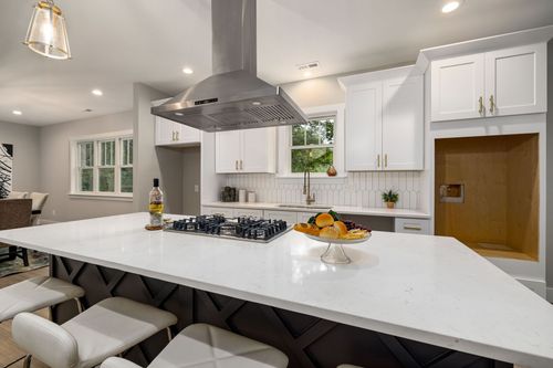 Bright modern kitchen with white island, stainless range hood, and stools beneath a large countertop.