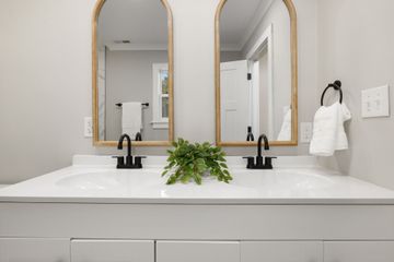 White bathroom vanity with two gold-framed mirrors, black faucets, and a small green plant centerpiece