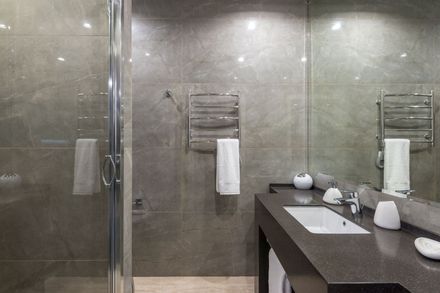 Modern bathroom with glass shower, gray tile, and a double sink vanity with towels and toiletries