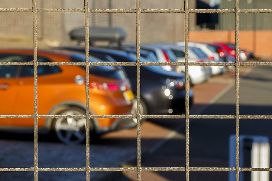 Orange car and other cars parked behind a metal grid fence.
