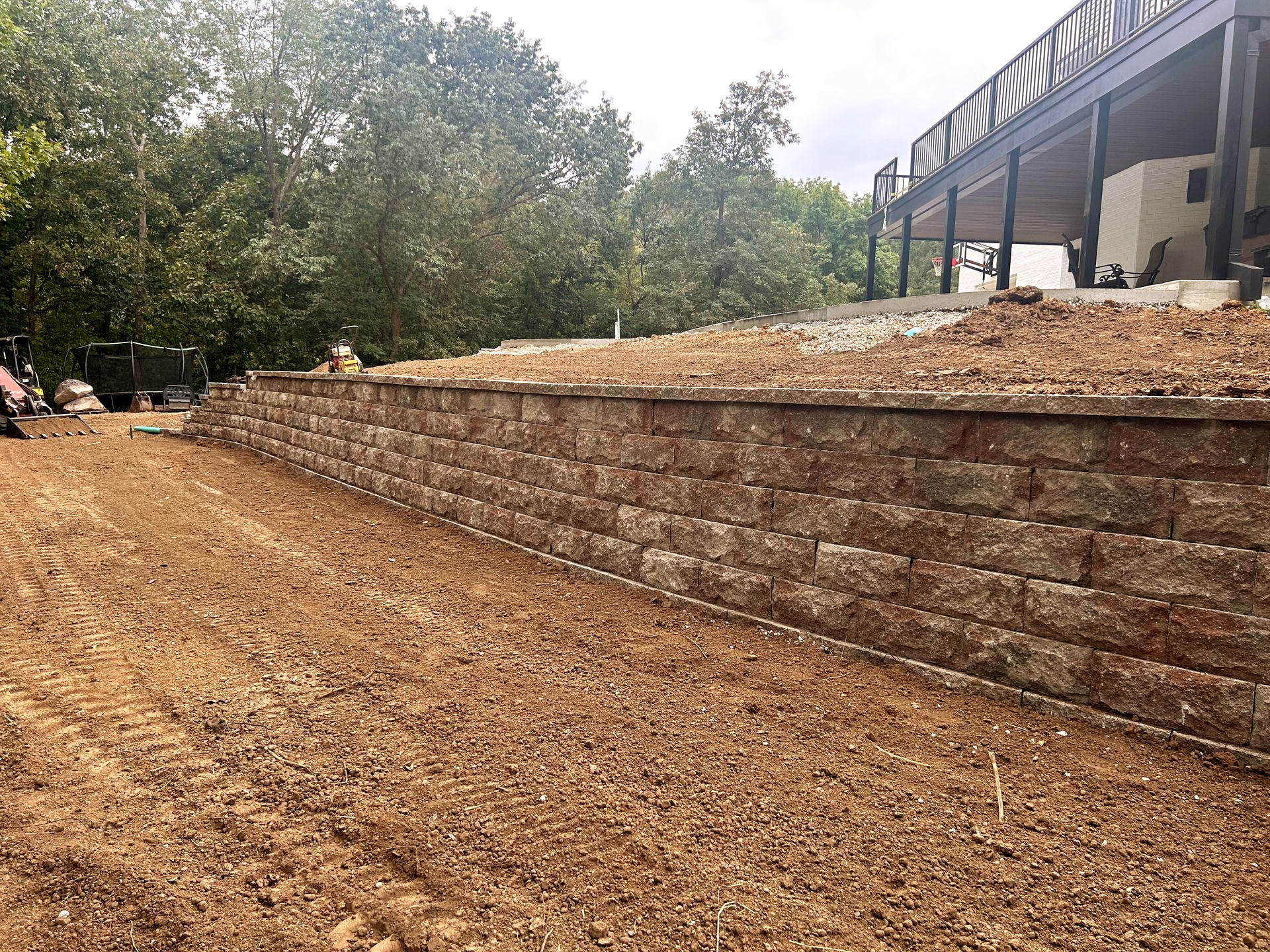 Terraced retaining wall beside a dirt slope next to a house and trees