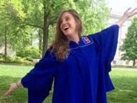 a woman in a blue gown is standing in a park with her arms outstretched .