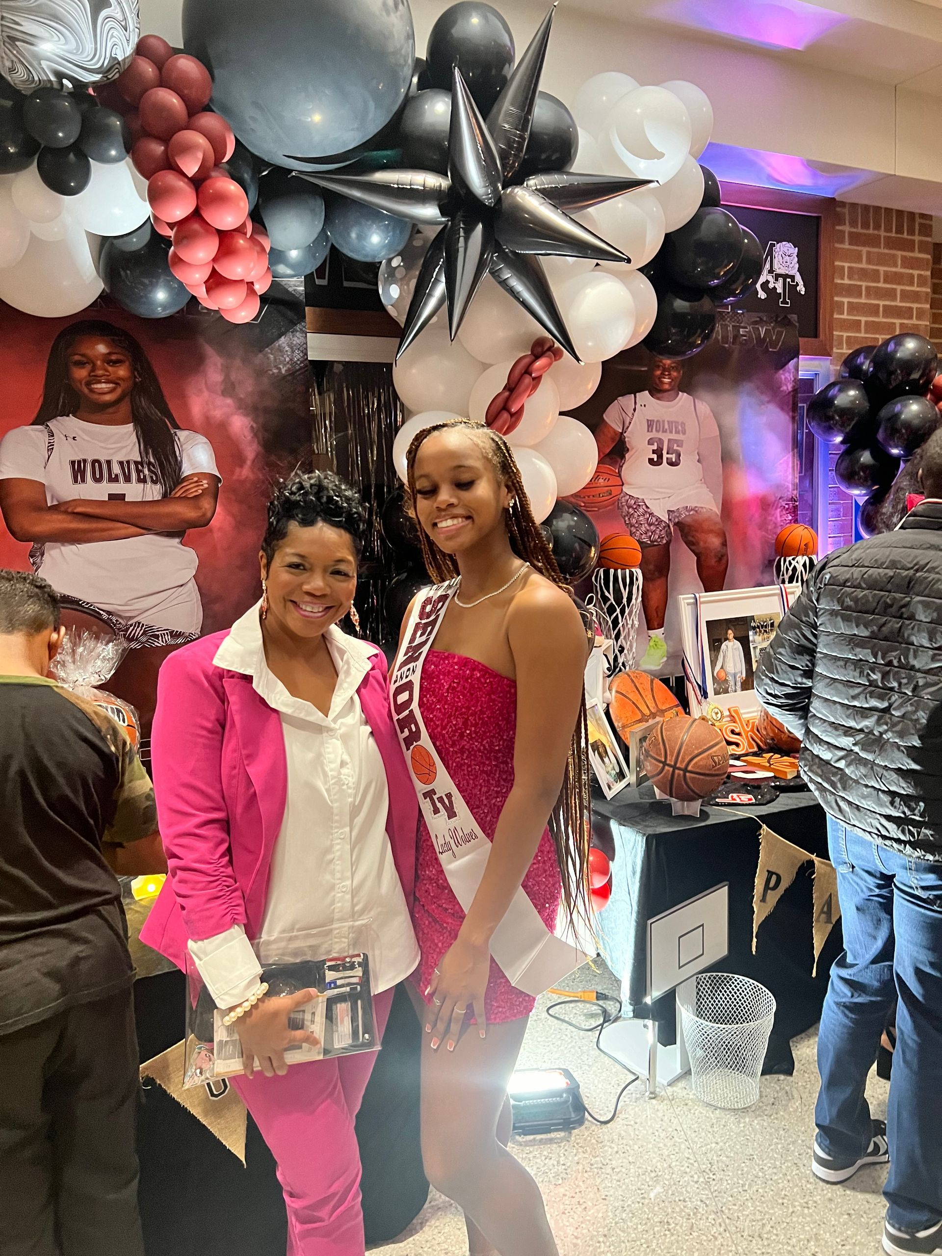 two women are standing next to each other in front of balloons and a basketball .