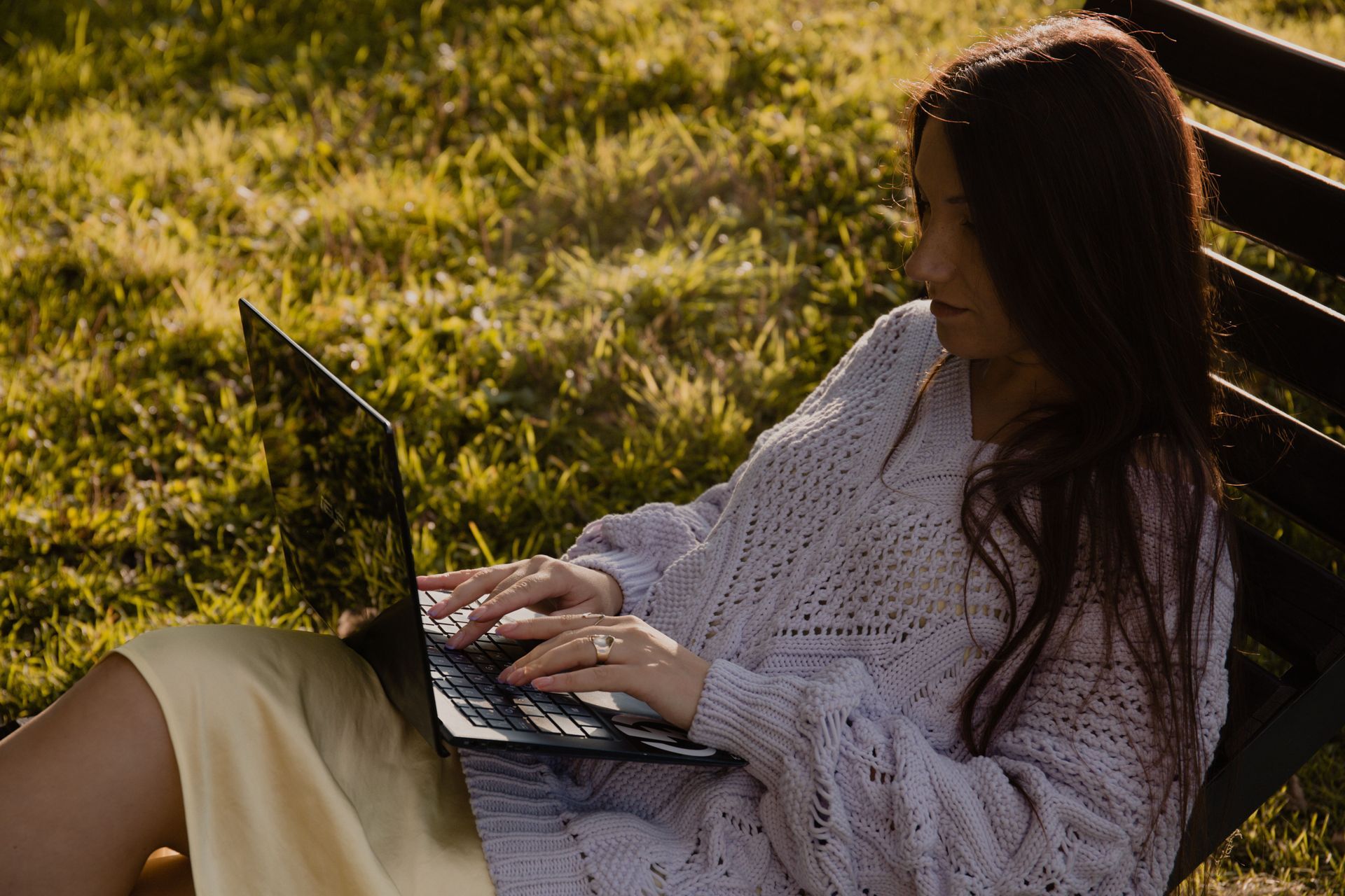 Young woman sits outdoors typing on her laptop.