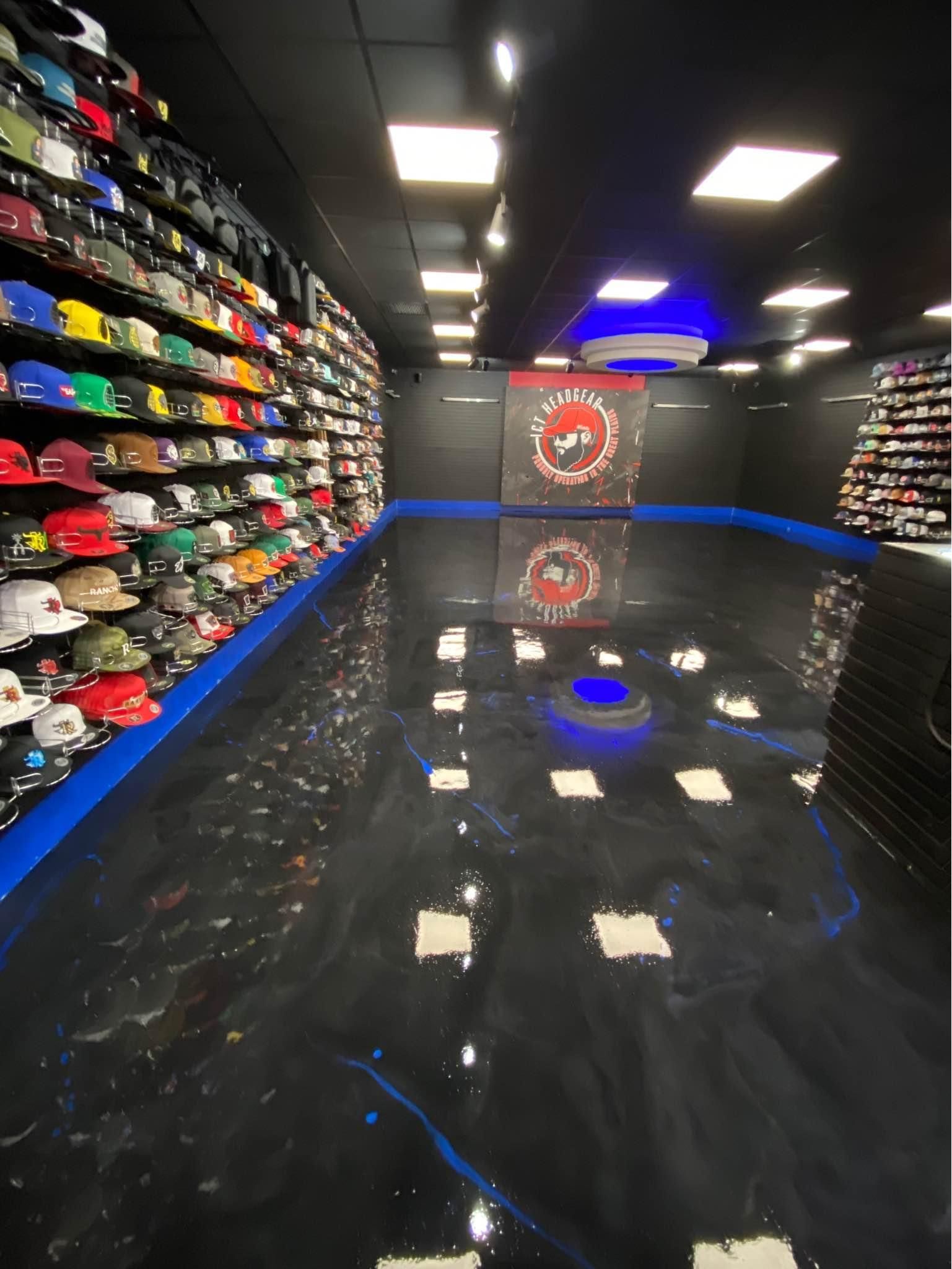 A retail store with epoxy flooring featuring a high-gloss, black finish with blue accents. The store has walls lined with rows of colorful hats and a central display area with overhead lighting reflecting on the polished floor.