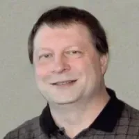 Smiling man in a black collared shirt against a plain light background