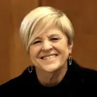 Smiling woman with short blonde hair wearing a black top against a warm brown background