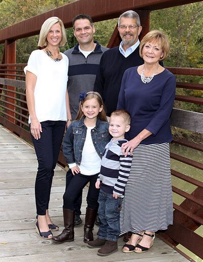 Family of five posing on a wooden bridge, dressed casually and smiling.