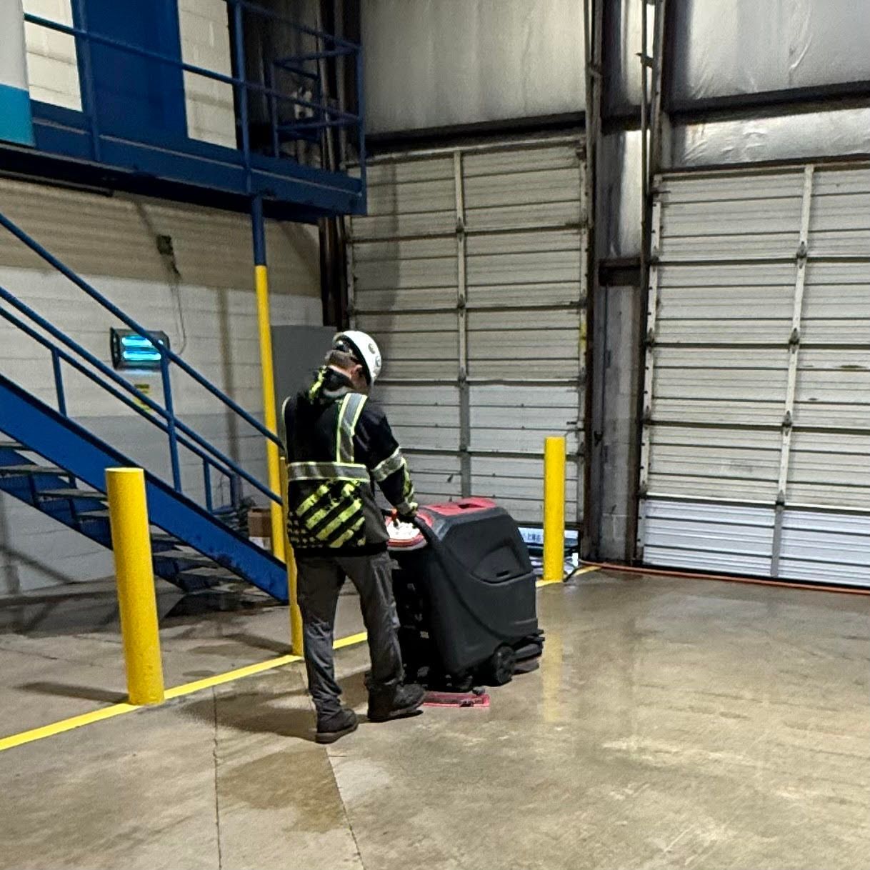 Person using an orange floor buffer machine to clean a shiny floor in a building.