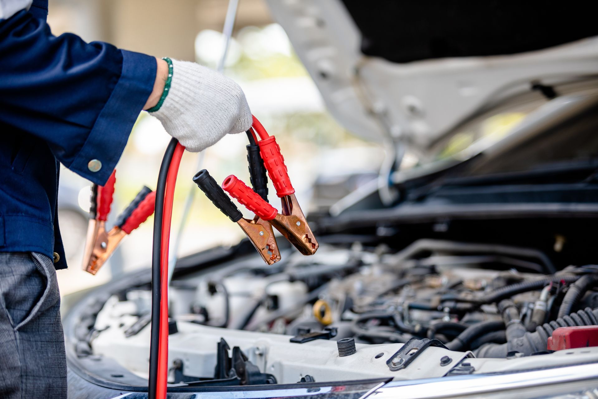 Mechanic using jumper cables on a car battery with the hood open