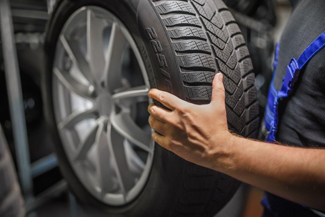 Mechanic holding a car tire beside a silver wheel in a garage