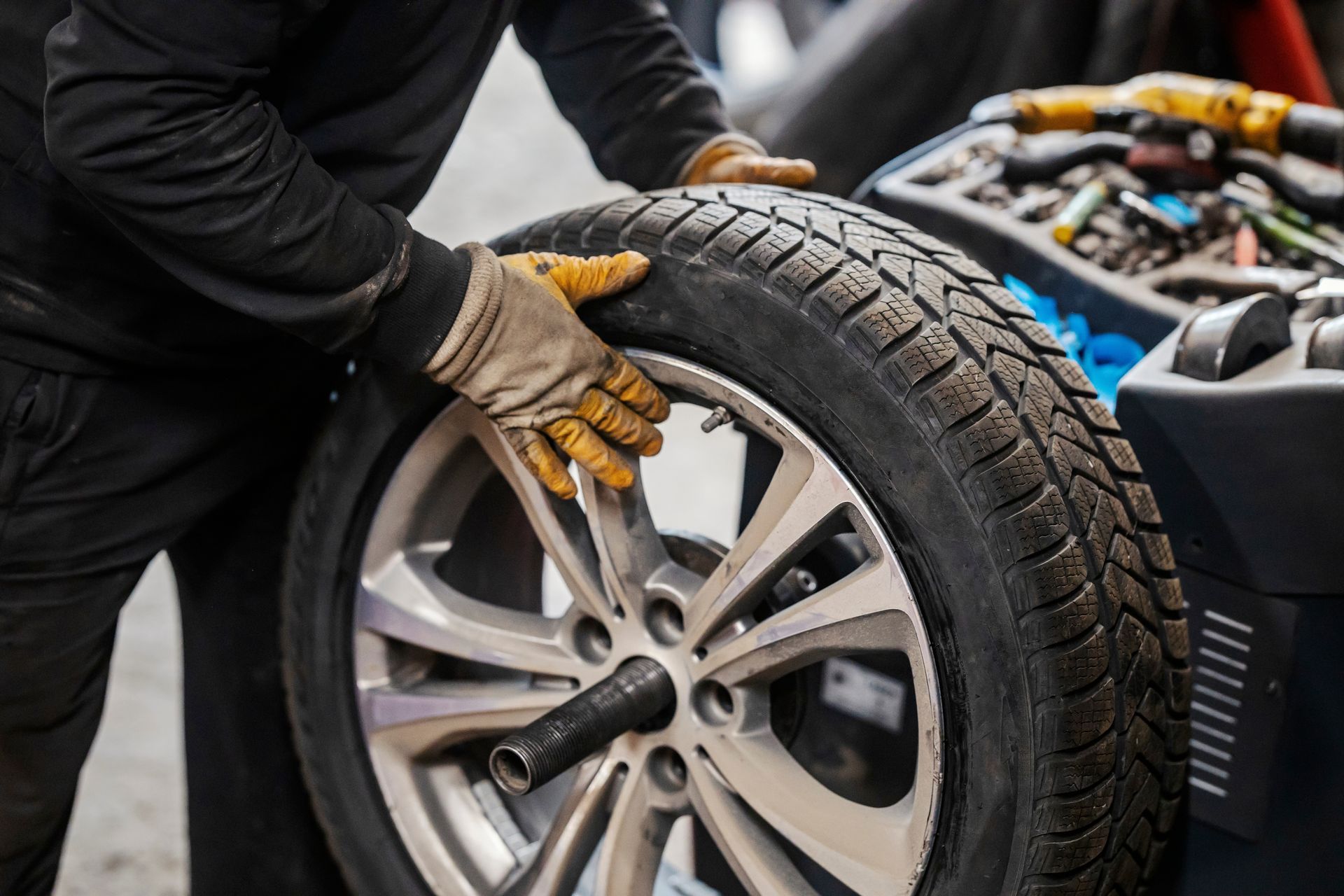 Mechanic wearing gloves changing a car tire with a wrench in a workshop