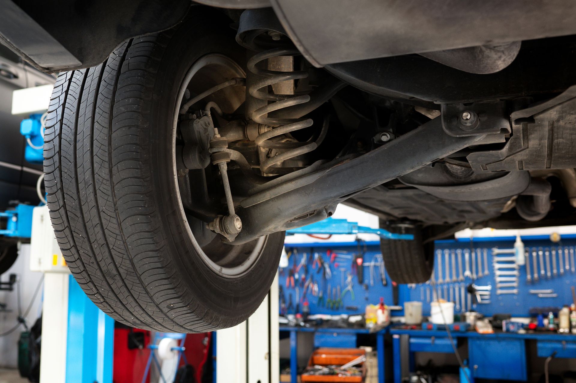 Car under a lift in an auto repair shop, showing the undercarriage and rear wheel.