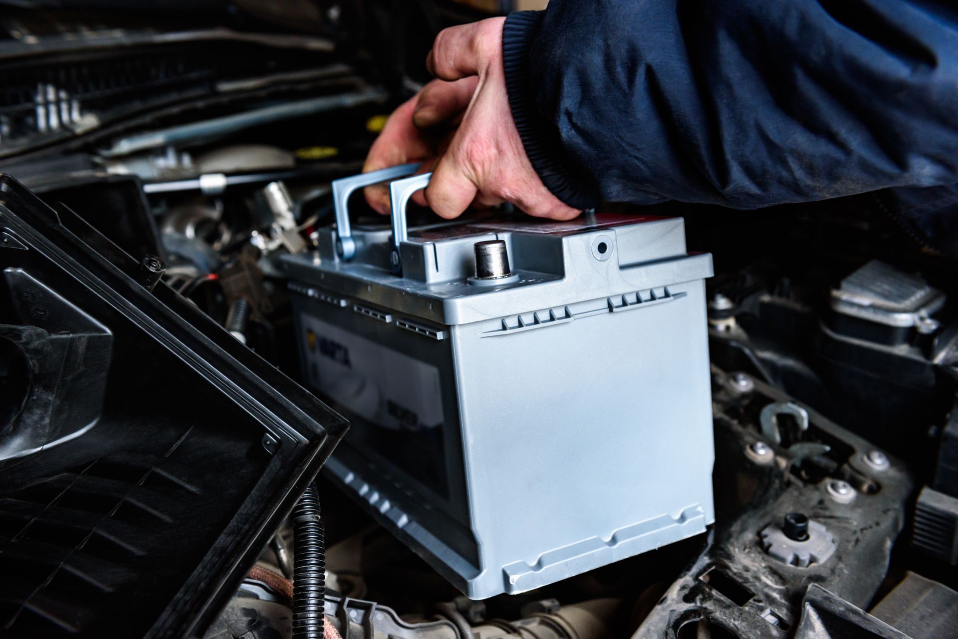 Hand placing a gray car battery into an engine bay under the hood