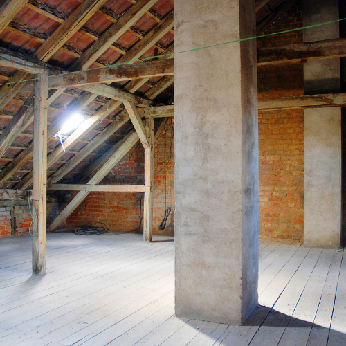 Attic interior with exposed brick walls, wooden beams, and a concrete pillar.