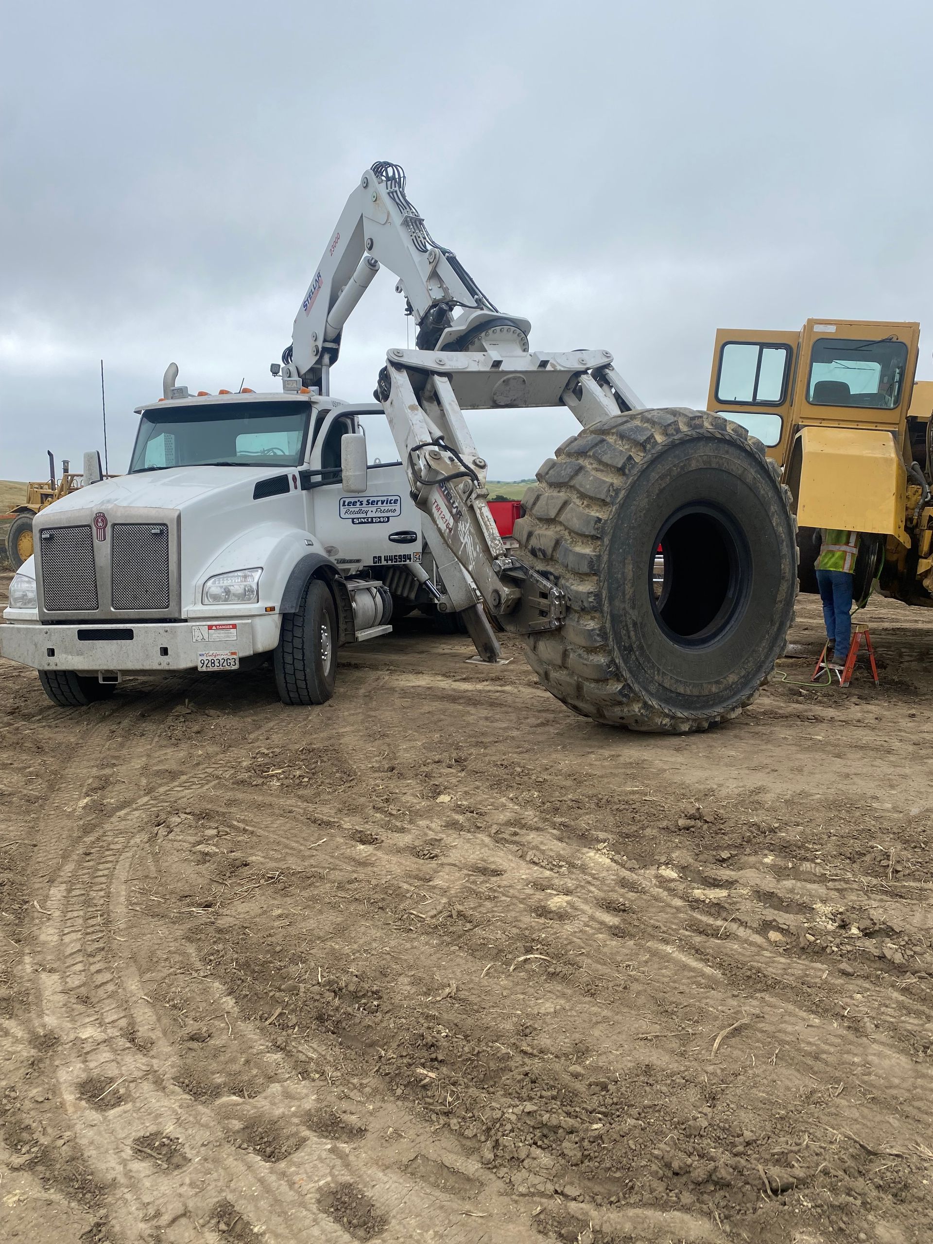 A large tire is being removed from a truck in a dirt field