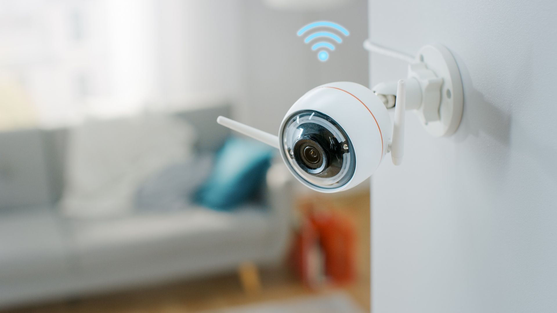 A white security camera with a wireless antenna mounted to an indoor wall, with a blue Wi-Fi signal icon floating above.