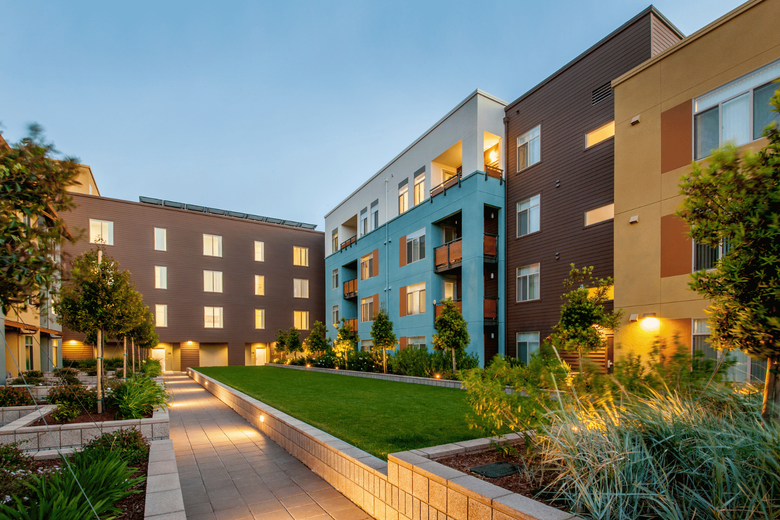 Modern apartment courtyard with lit walkways, green lawn, and brick-and-blue buildings at dusk