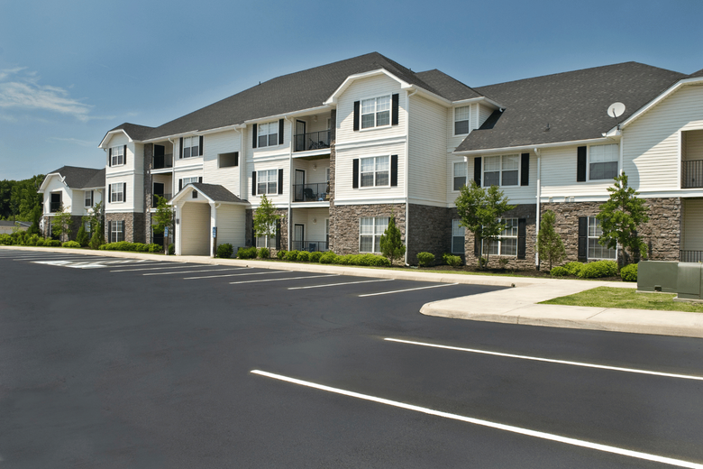 Modern apartment complex with beige siding and stone accents along a paved driveway