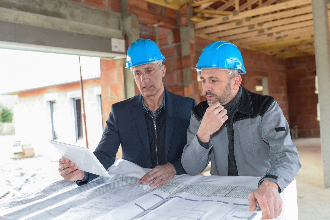 Two construction workers in blue hard hats reviewing blueprints at a building site