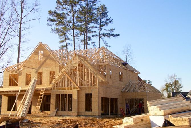 Wood-framed house under construction with ladders and scaffolding on a sunny site