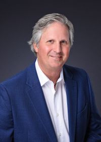 A man in a blue suit and white shirt is smiling for the camera.