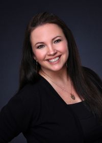 A woman wearing a black shirt and a necklace is smiling for the camera.