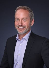 A man in a suit and purple shirt is smiling for the camera.