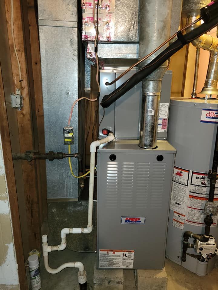 A furnace is sitting in a basement next to a water heater.