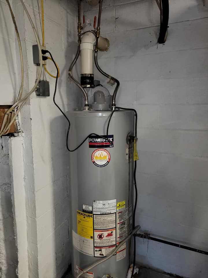 A water heater is sitting in a basement next to a wall.