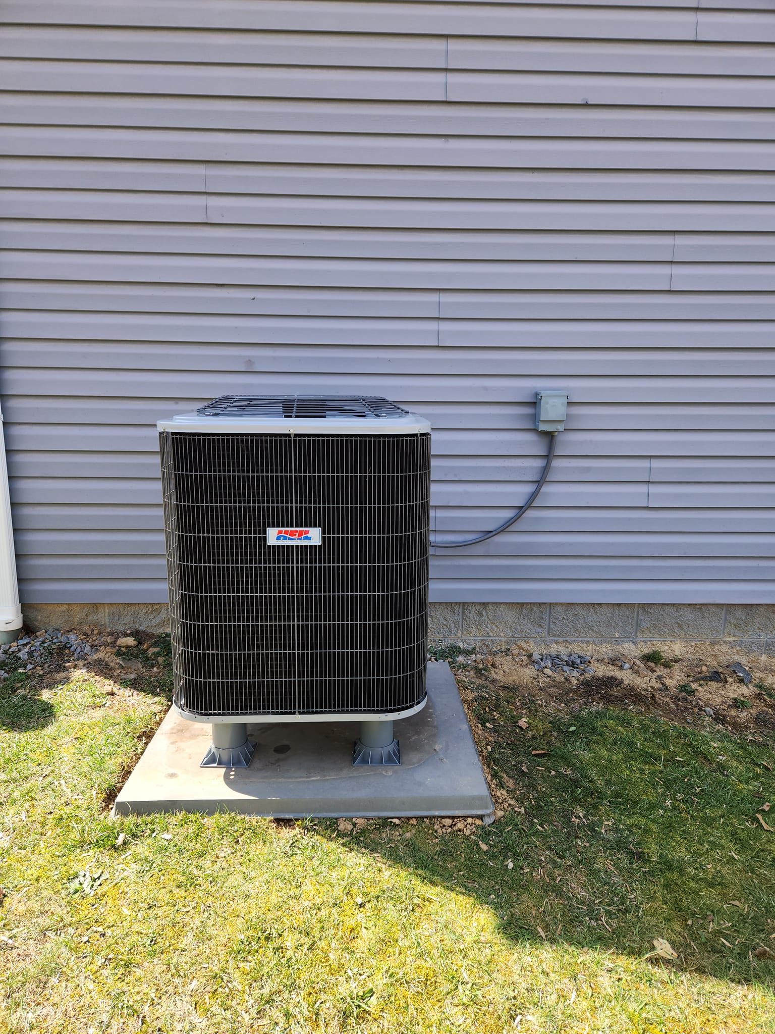 An air conditioner is sitting on a concrete platform in front of a house.