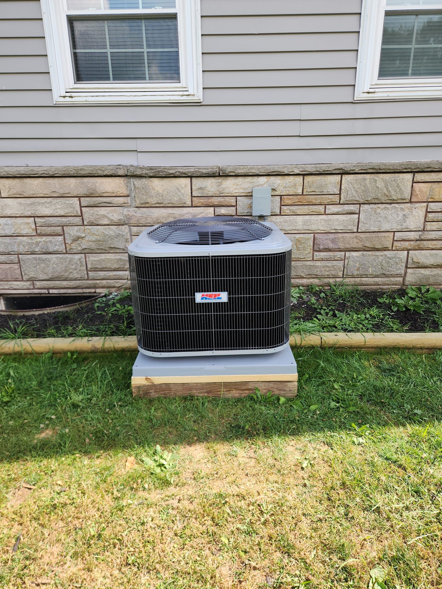 An air conditioner is sitting in the grass in front of a house.