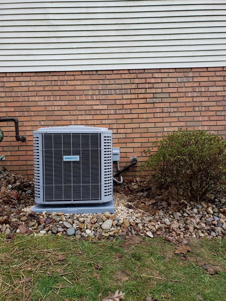 An air conditioner is installed on the side of a brick house.
