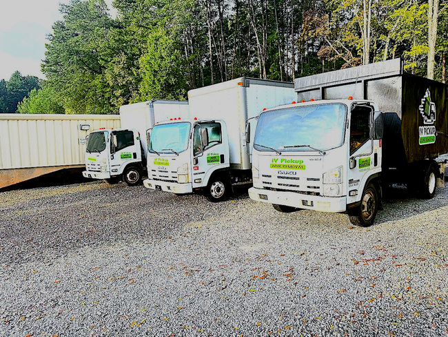 Three white utility trucks parked on gravel beside a tan building and trees.