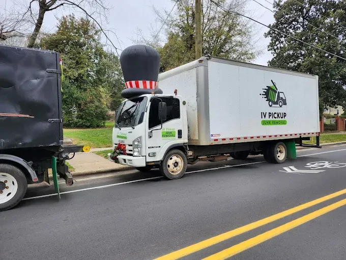 White box truck with oversized hat decoration parked on a street beside another truck.