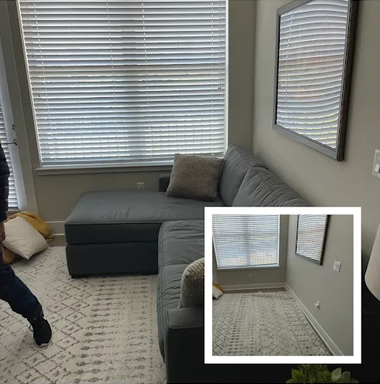 Small living room with gray sectional, patterned rug, window blinds, and a mirror on the wall.