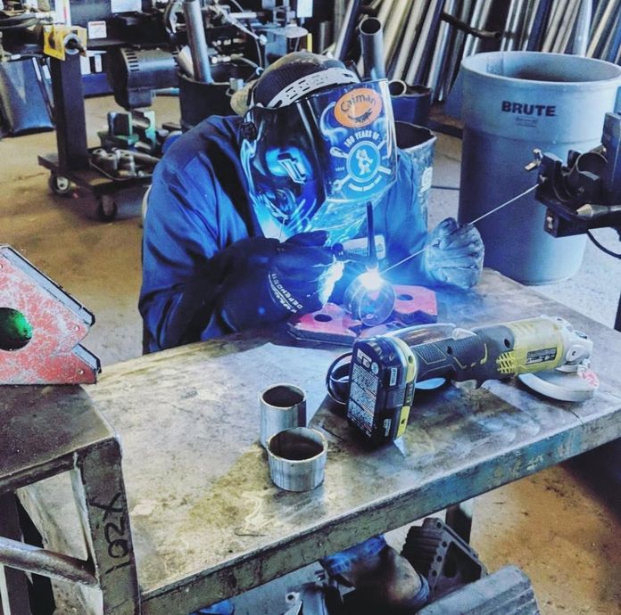 Welder in blue jacket and helmet welding metal on a workbench, bright blue arc light in workshop