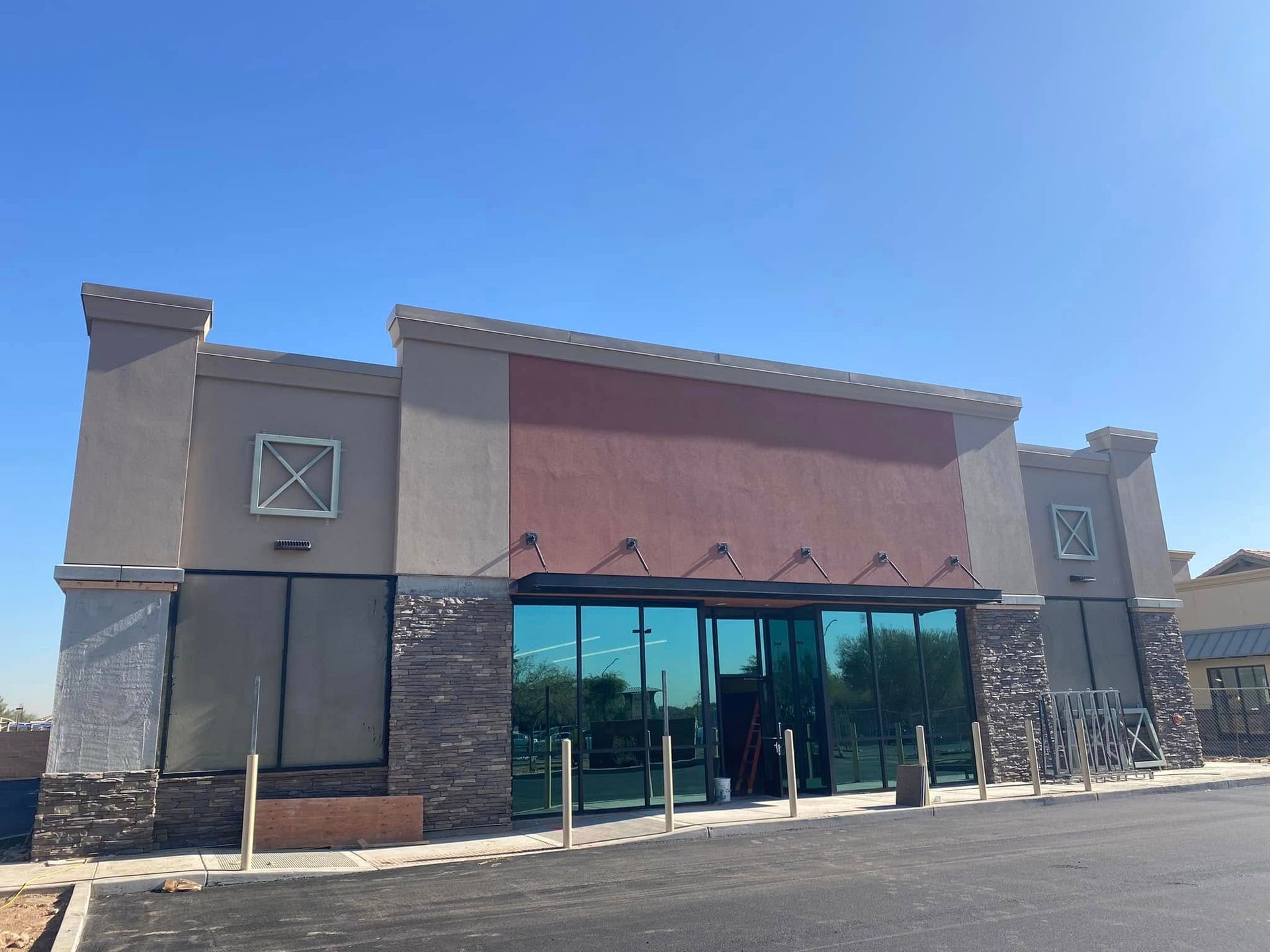Single-story storefront with large glass entrance, stone accents, and a clear blue sky.