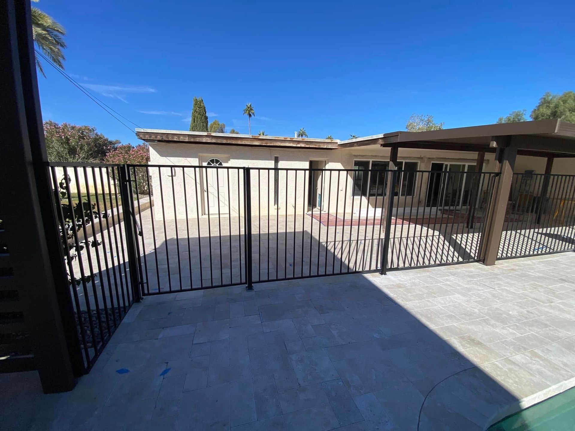Black metal gate on a sunny patio with a house and fenced yard beyond