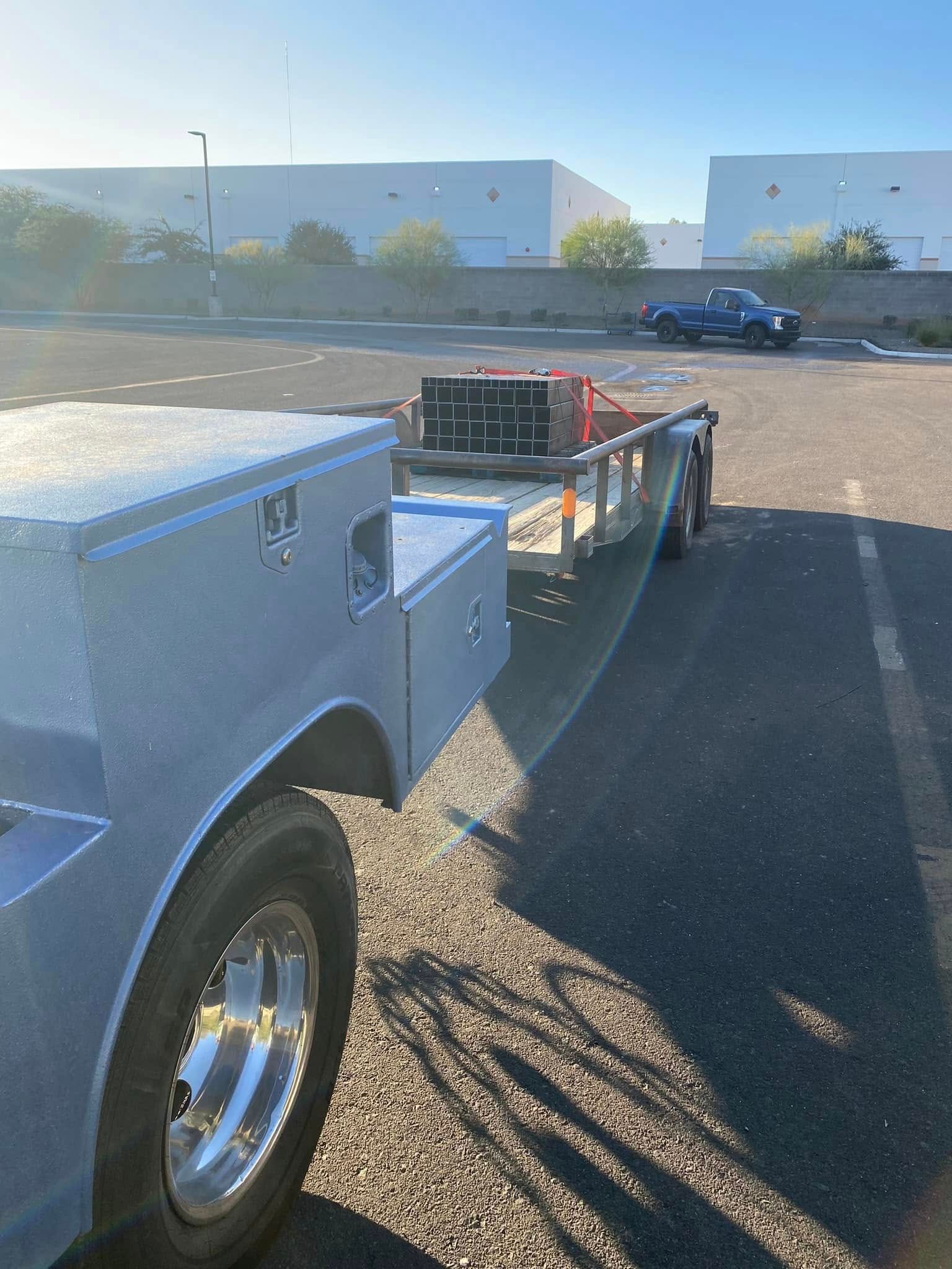Silver pickup truck towing a flatbed trailer in a sunny parking lot