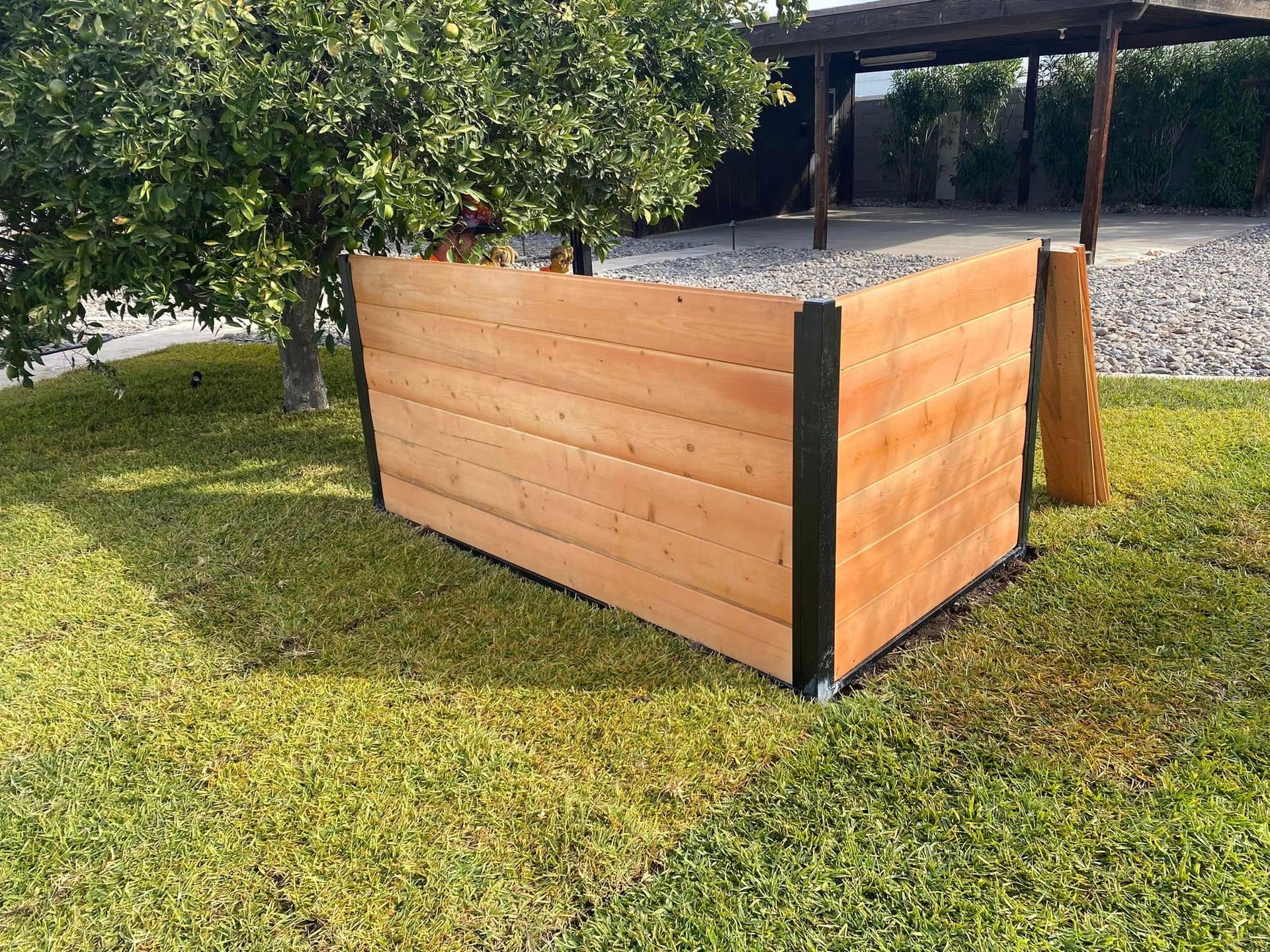 Wooden raised garden bed on grass near trees and a patio cover