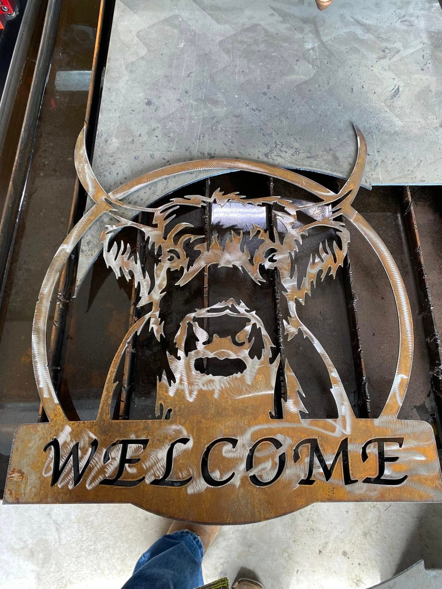 Rustic metal welcome sign with a bull skull and horns, mounted on a gray wall.