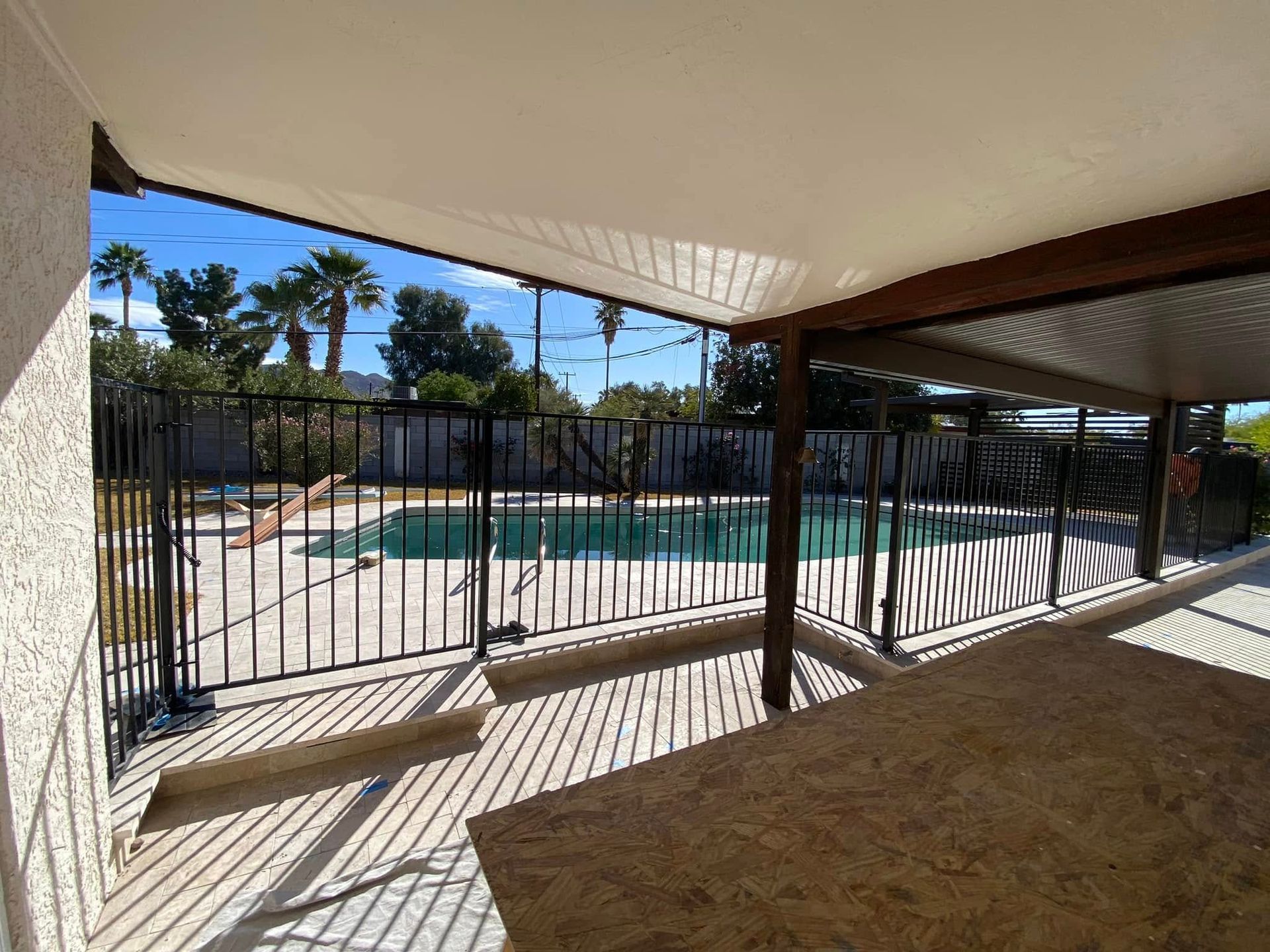 Covered patio overlooking a fenced backyard pool, with lounge chairs and sunny shadows.